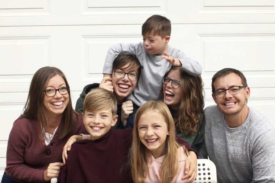 family of 7 filled with laughter in matching maroon and grey shirts by garage door