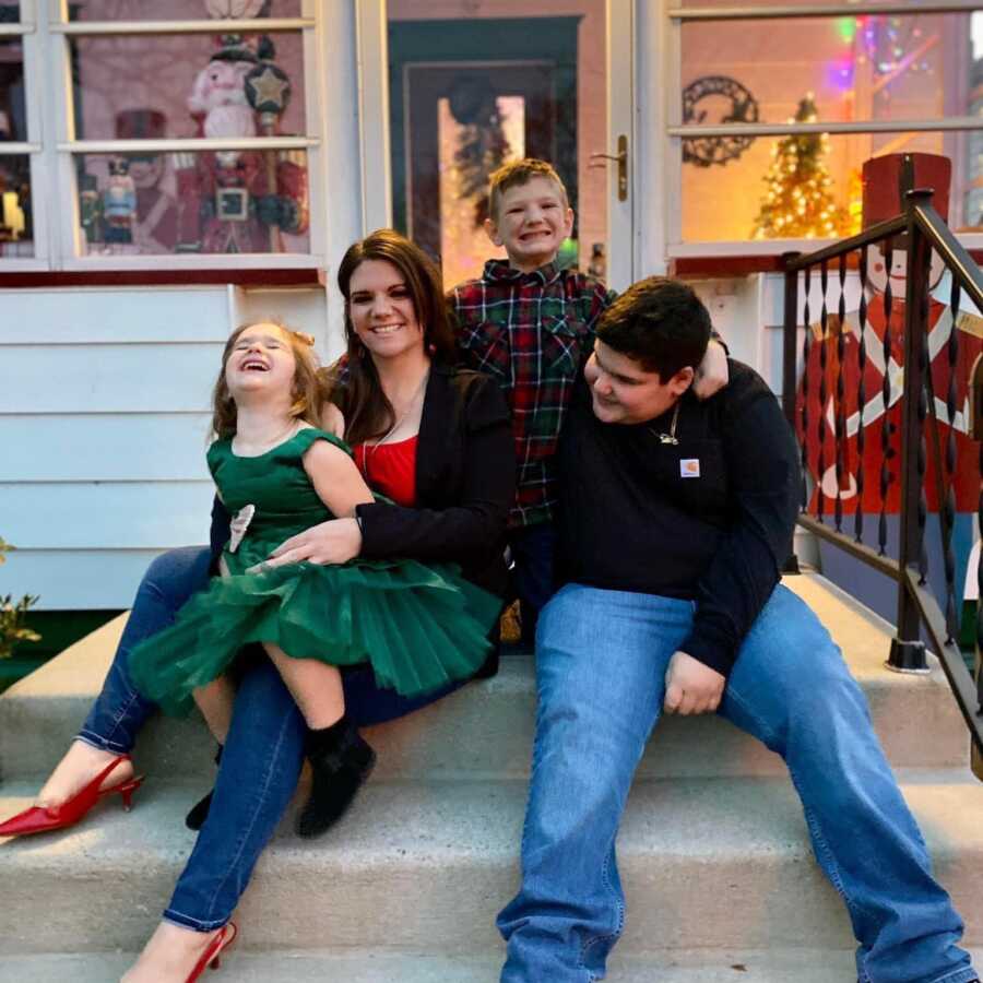 Mom, daughter, and two sons sitting on porch of house for family photo
