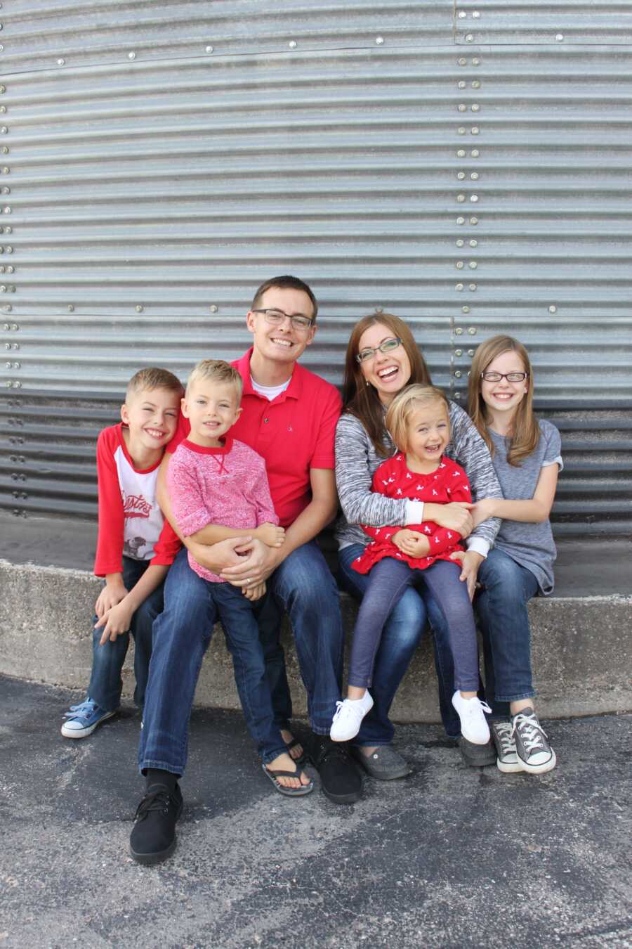family of 7 in matching red and grey shirts sitting on concrete bench
