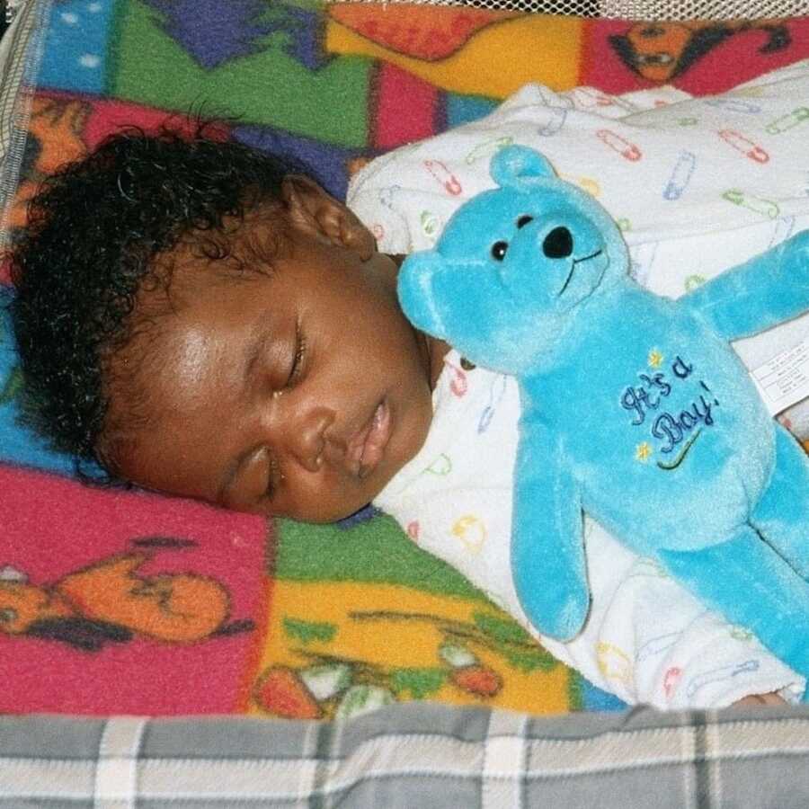 infant boy who was adopted sleeps with teddy bear on his chest