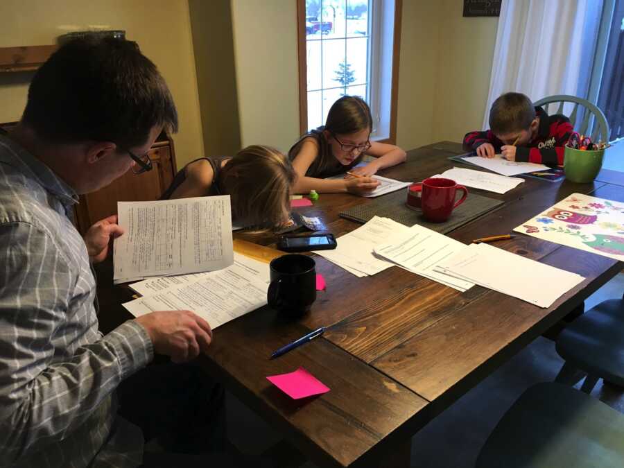 family sitting at dining table filling out adoption paperwork for son with Down syndrome