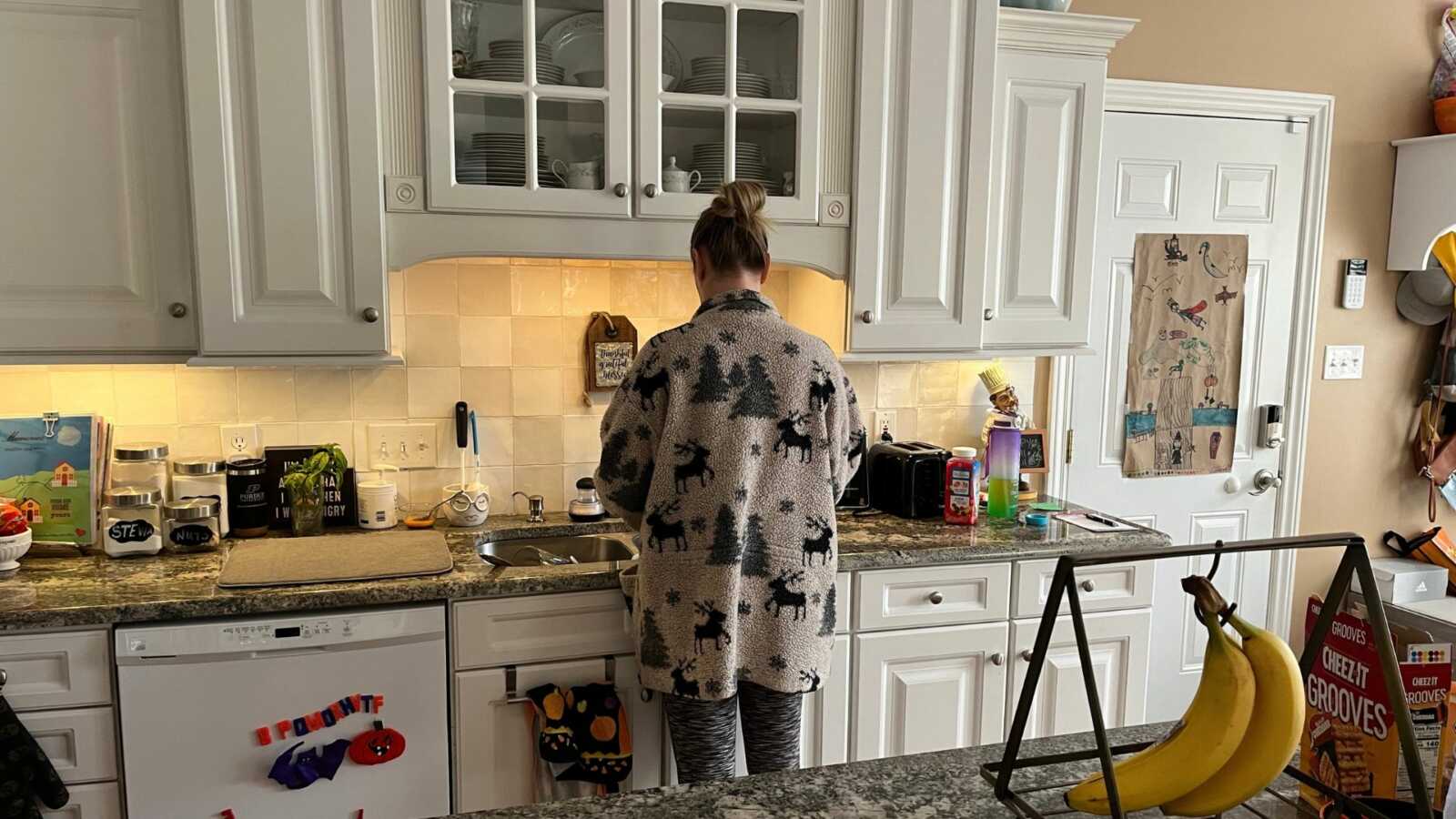 mom standing in kitchen wearing oversized Christmas sweater with back turned to camera