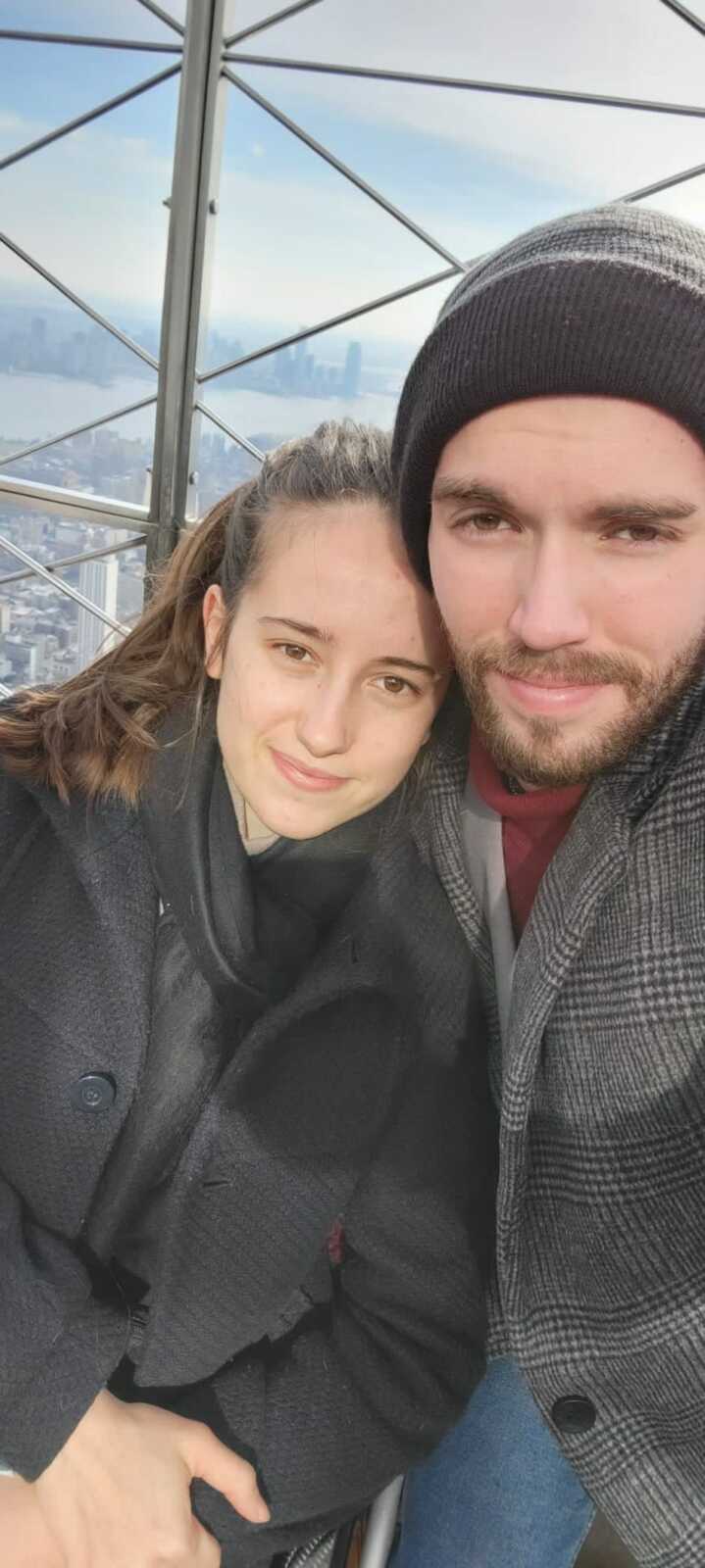 Paraplegic Woman in black scarf and coat next to husband at top of sky scraper