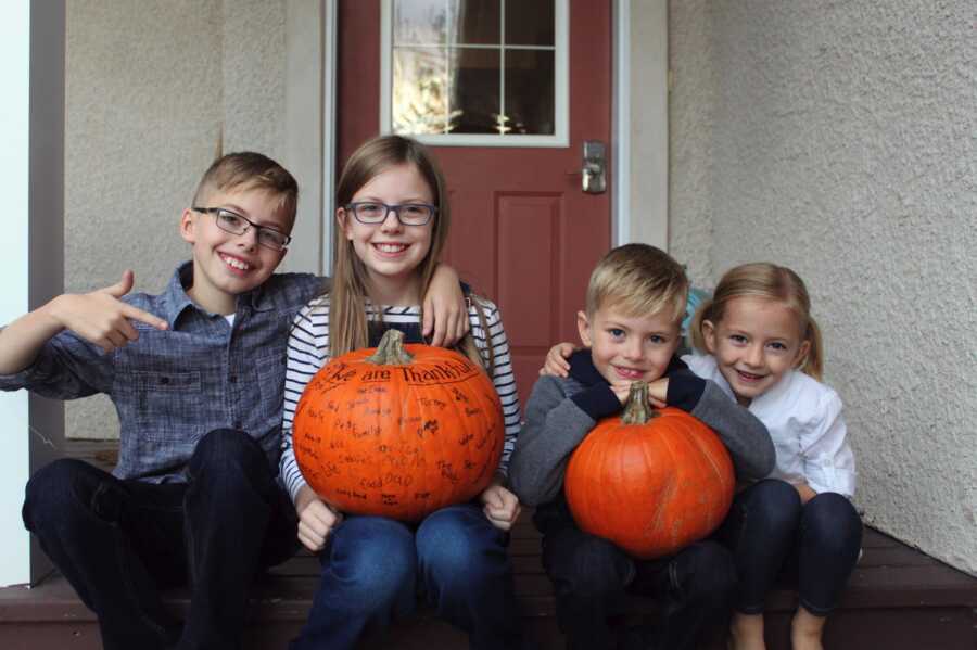 4 siblings sitting on front porch with orange pumpkins in lap