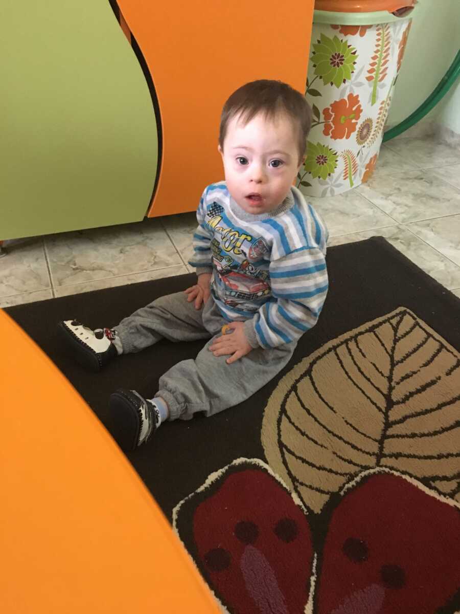 adopted son with Down syndrome sitting on brown carpet with leaf designs