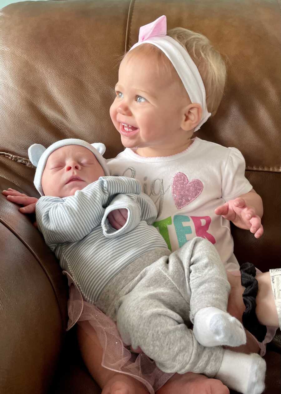 toddler sister sitting with newborn baby brother sleeping in lap