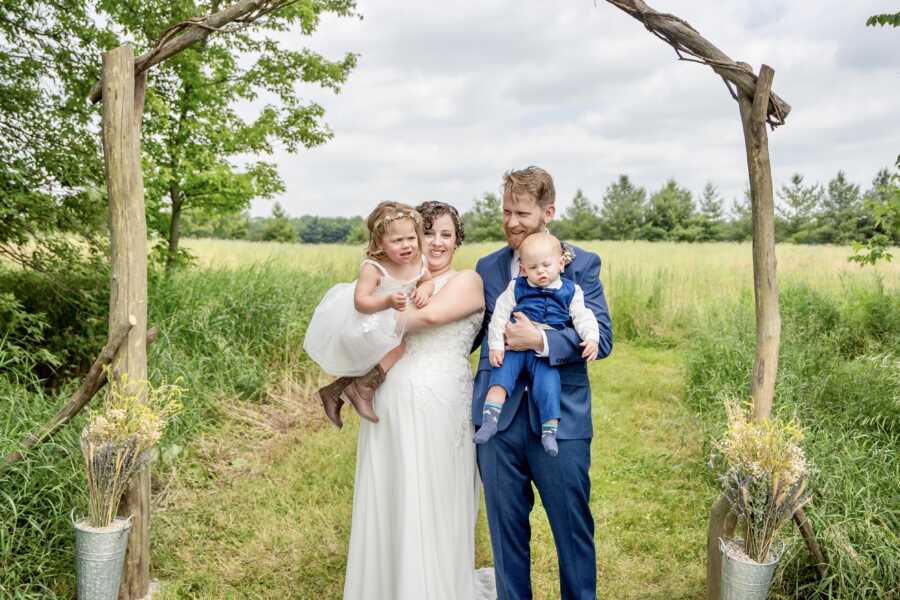 adoptive mom getting married to partner under wedding arch with adoptive children 