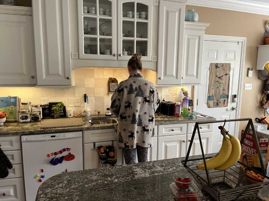 mom standing in kitchen wearing oversized Christmas sweater with back turned to camera