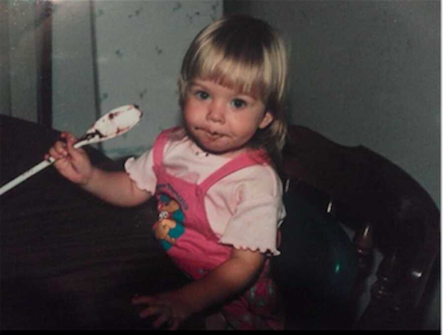 young girl sitting holding a spoon with batter on it