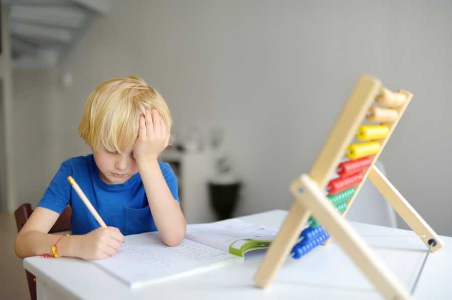 young boy sits at desk completing school work