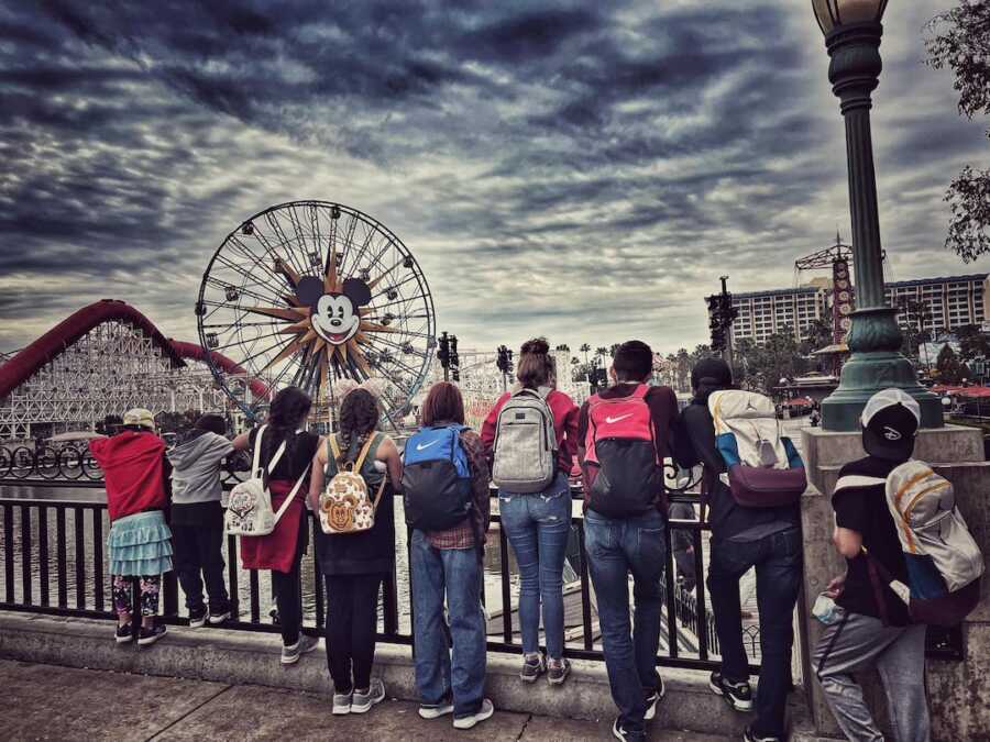 foster children standing in a line on a railing in Disneyland overlooking rides