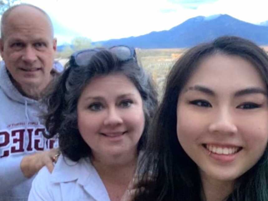 Chinese adoptee takes a selfie in front of mountains with her adoptive parents