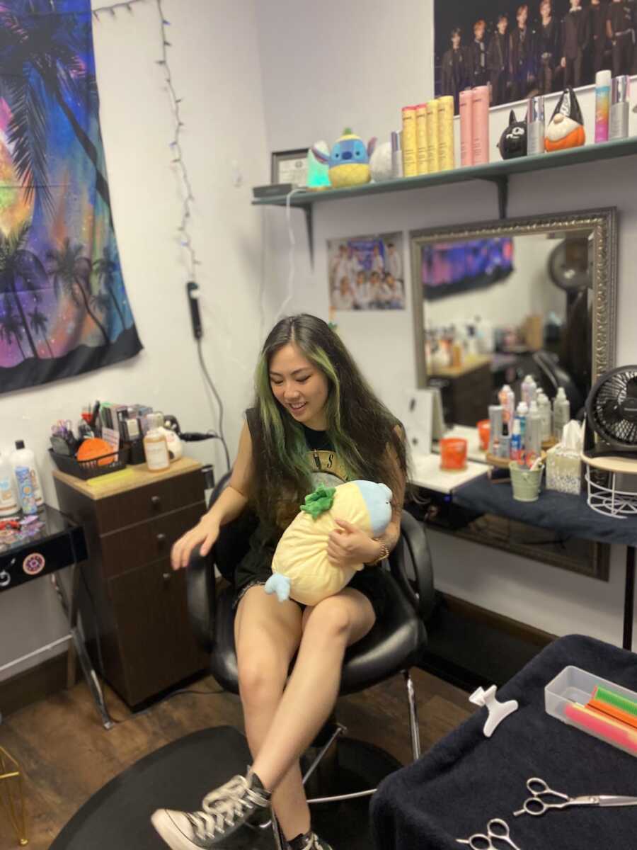 Chinese adoptee sits in hairdressing chair holding a plush stuffed animal