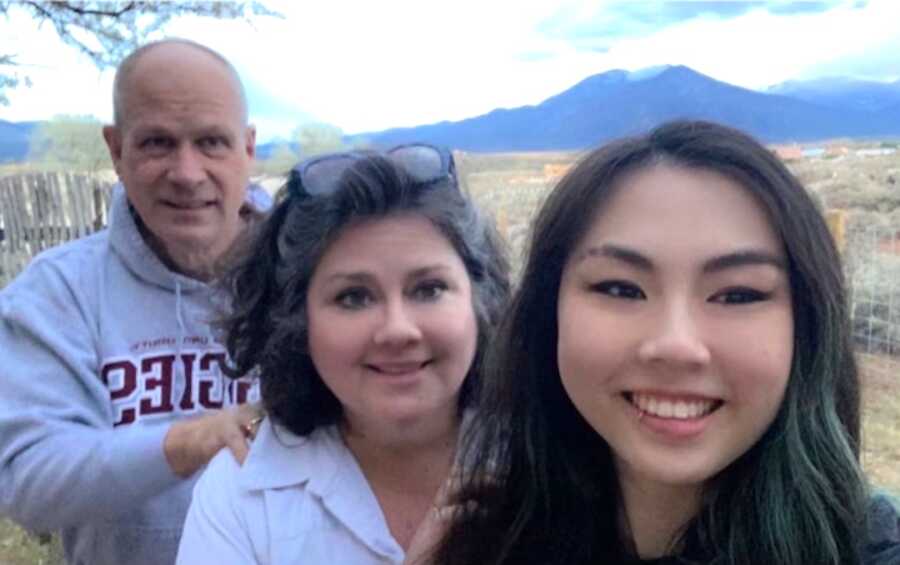 Chinese adoptee takes a selfie in front of mountains with her adoptive parents