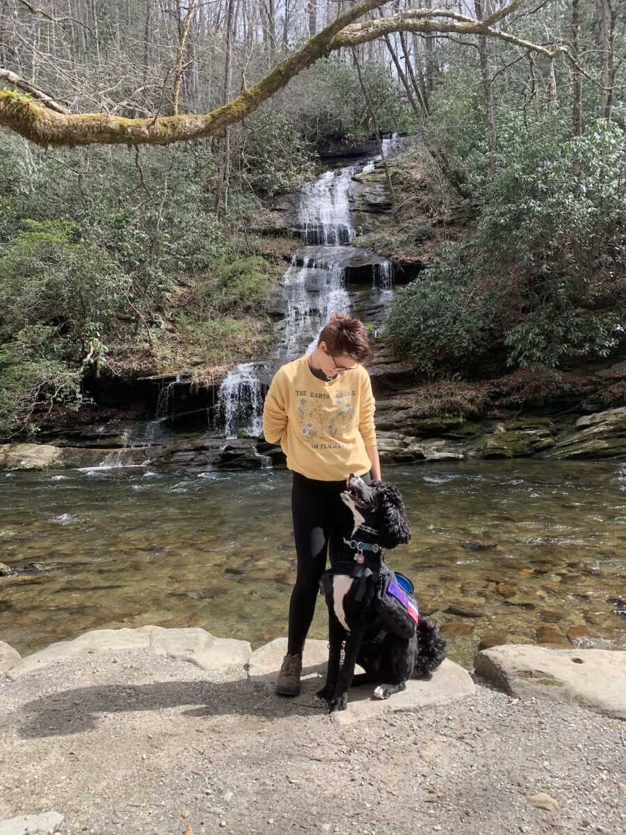 woman with Ehlers-Danlos syndrome looks down at her service dog while by a waterfall