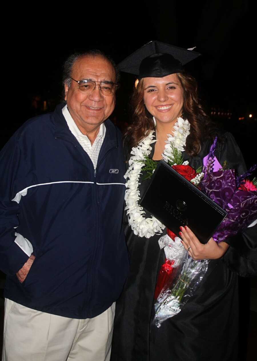 college graduate stands in cap and gown with her grandfather