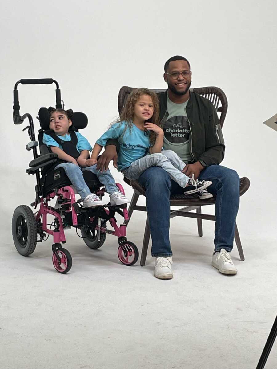 Dad with special needs daughter with other daughter on his lap for photoshoot