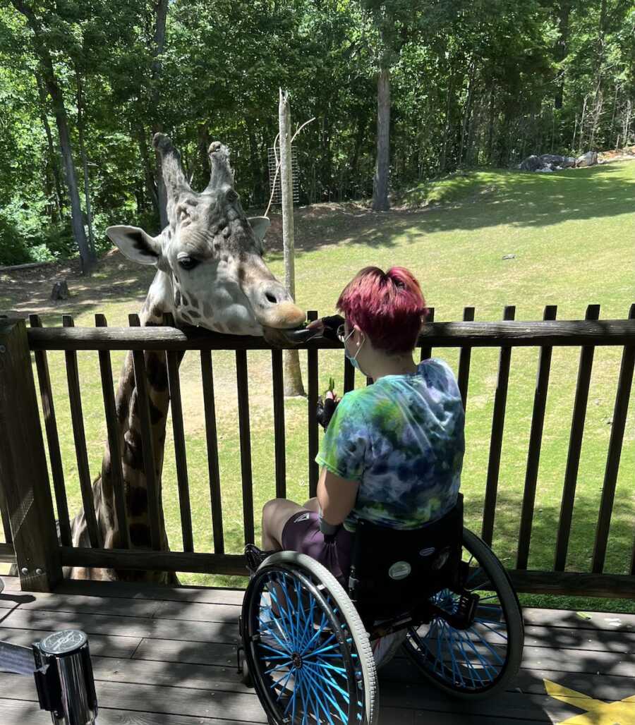 woman with Ehlers-Danlos syndrome in wheelchair feeding a giraffe 