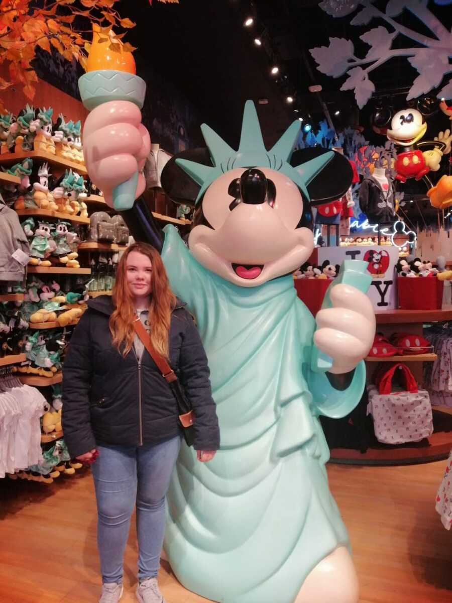 epileptic woman stands next to mickey mouse statue dressed as Statue of Liberty