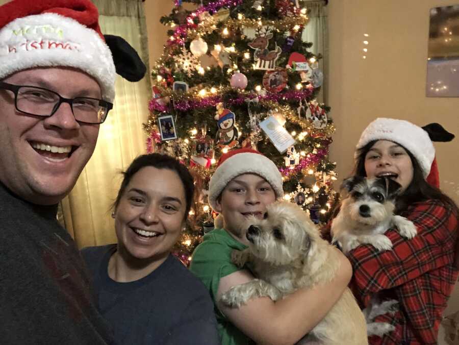 mom, dad, two children, and dogs taking a selfie in front of their Christmas tree