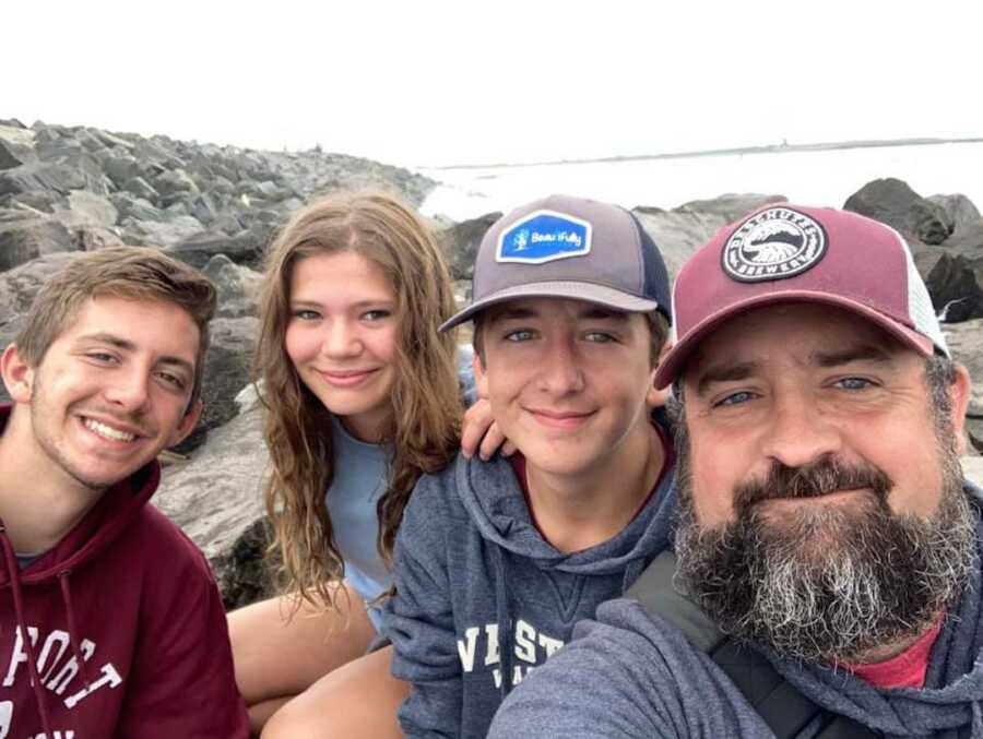 father taking a selfie with two sons and daughter on rocks by the water