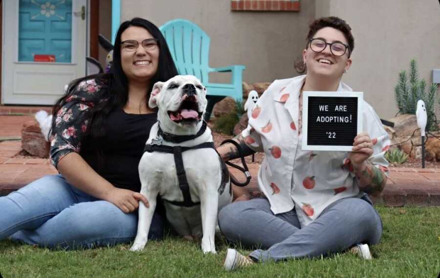 lgbtq+ couple sits with their dog holding sign announcing they are adopting