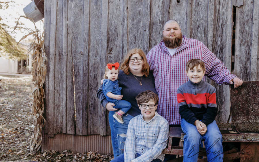 adoptive parents stand with their three children in front of barn