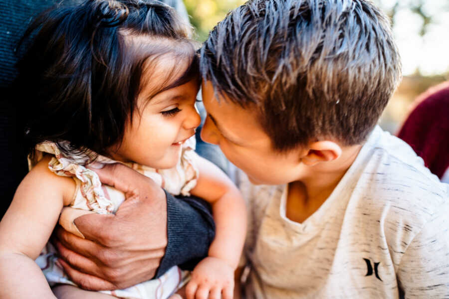 siblings look adorinlgy at one another with their foreheads pressed against each one another's