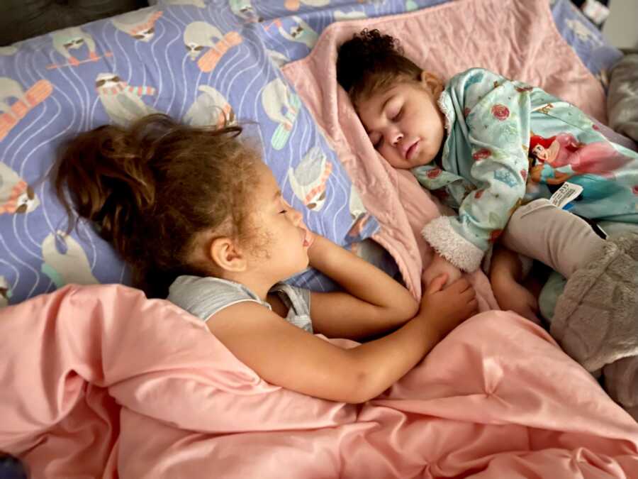 special needs daughter sleeping next to younger sister in bed