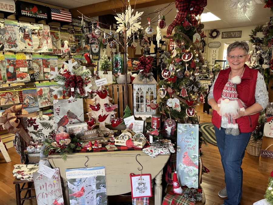 Small business owner in her Christmas decorations shop hiding a mini Santa