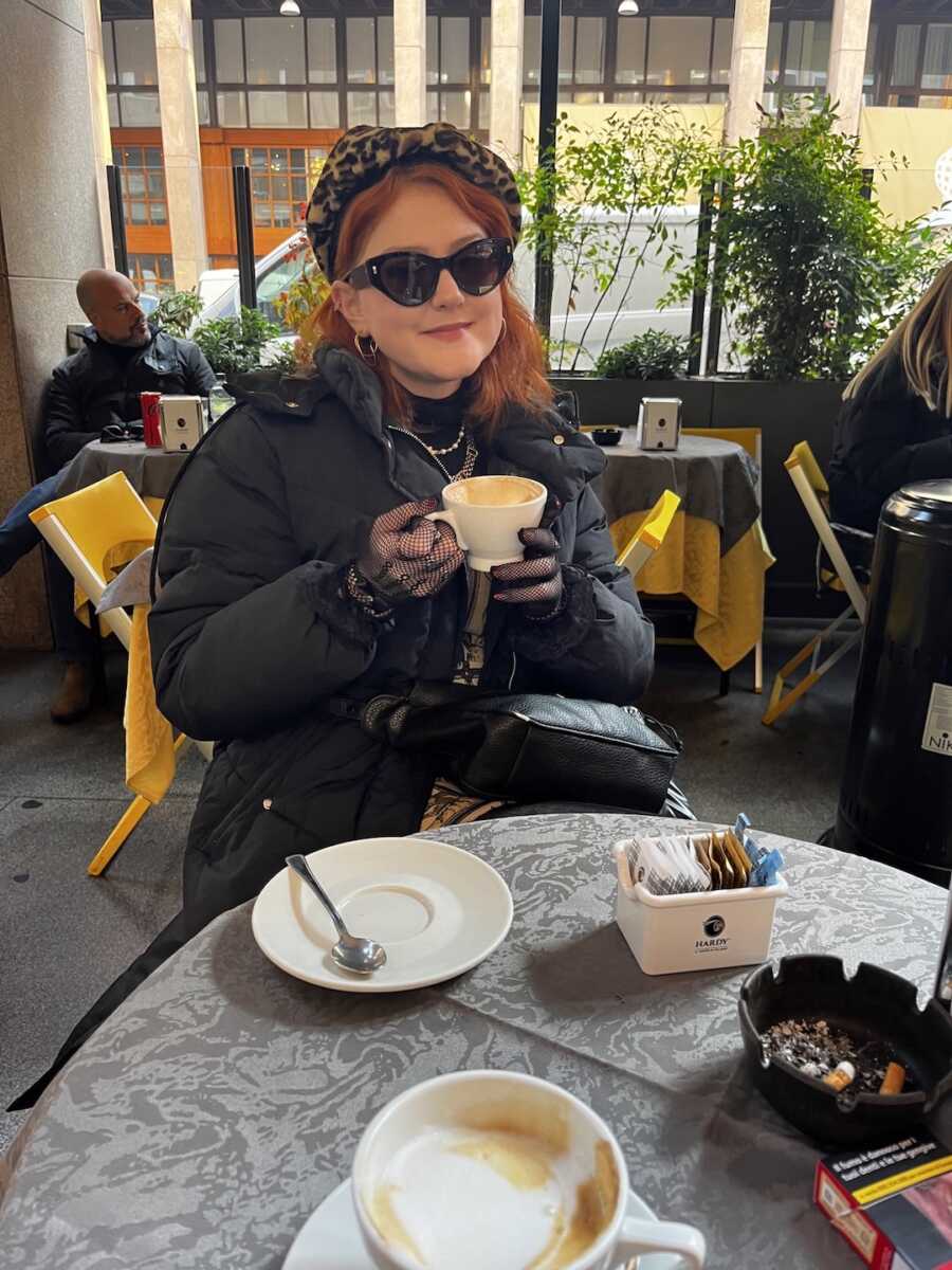 sober woman sitting at a table at a cafe holding a cup of coffee