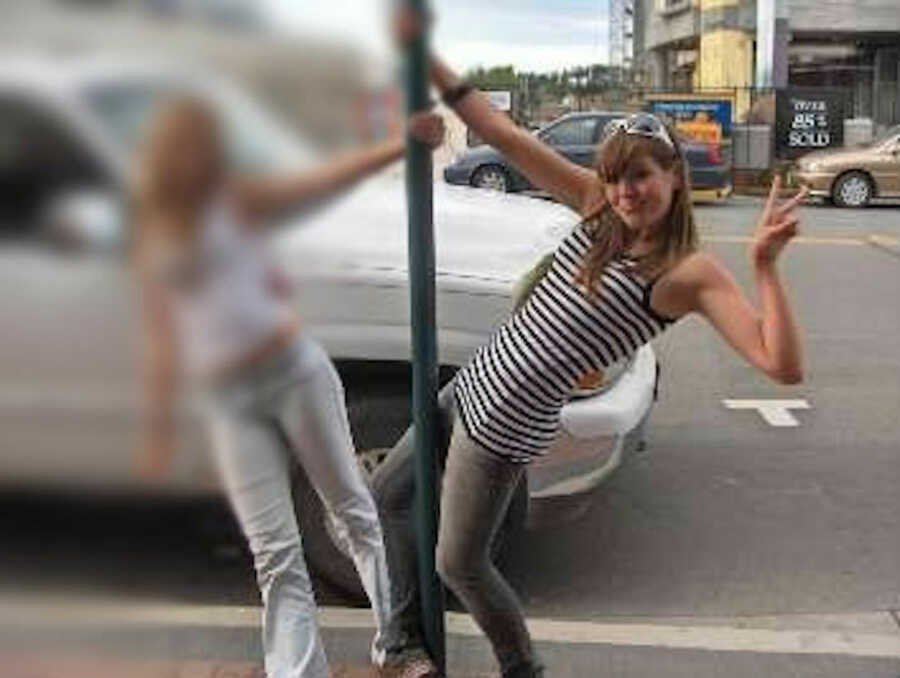 teenage girl struggling with body image hanging on green pole on sidewalk throwing up peace sign