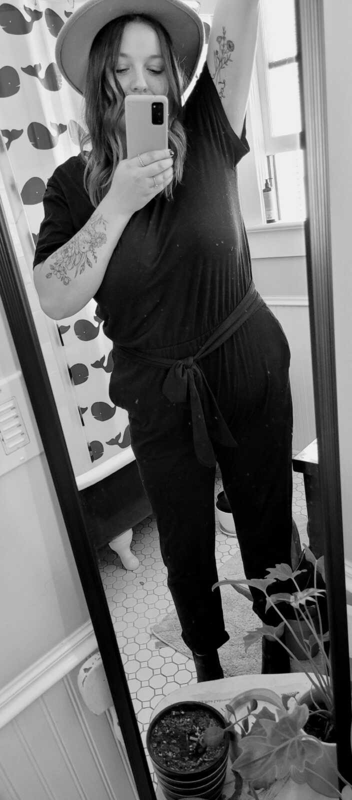 woman who struggled with body image wearing all black standing in long mirror
