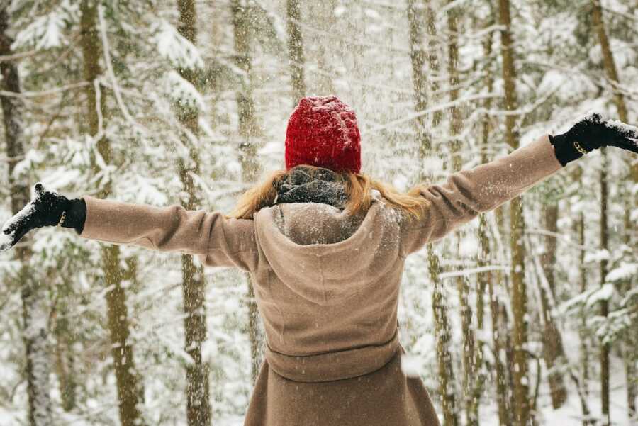 woman stands in a snowy forrest with arms out