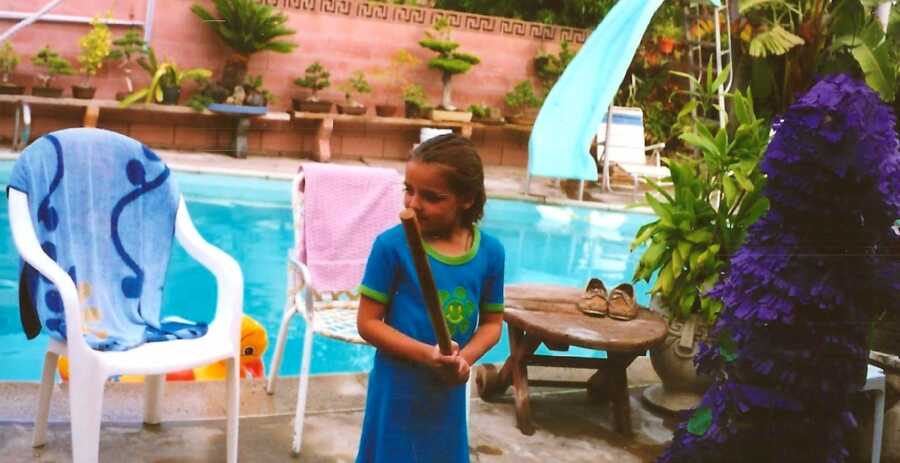 young girl standing in front of a pool while holding a bat
