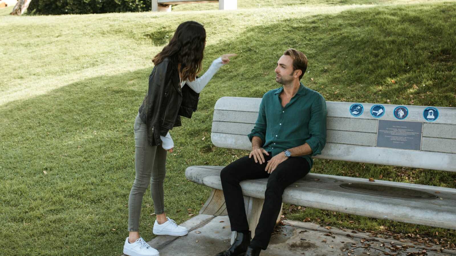 Woman angrily pointing at man on wooden bench