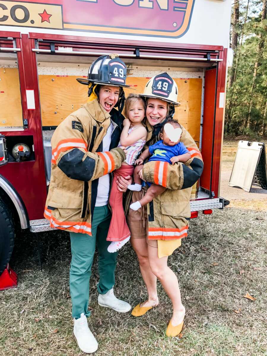 Family in firefighter outfits pose in front of a fire truck