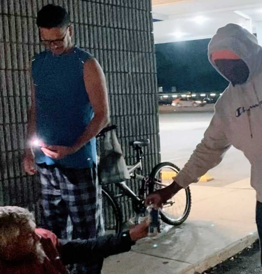 Hooded man offering homeless man a can of beer