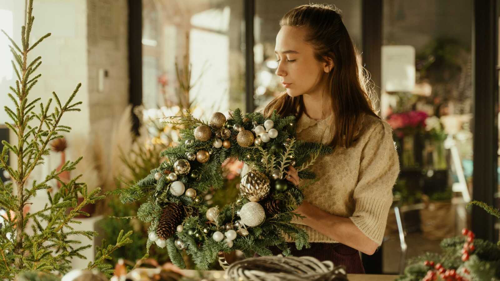 Woman in brown sweating holding Christmas wreath