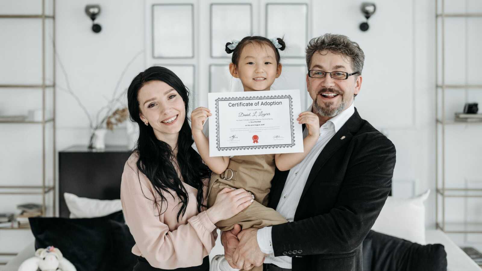 Adoptive parents hold their daughter and her adoption certificate